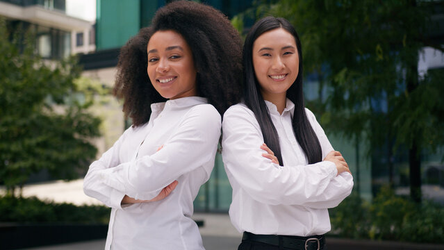 Successful Asian Korean African American women team arms crossed smiling girls businesswomen business outdoors multiracial colleagues confident posing employees partners city crossing hands females