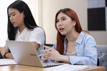 In a contemporary office environment, two women converse intently at table about work.
