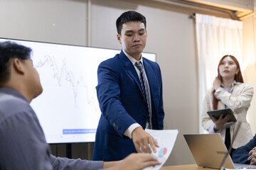 Group of professionals engaged in business meeting, discussing financial reports and charts while...
