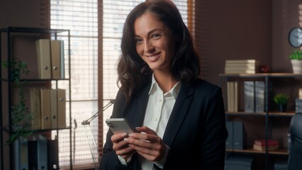 Caucasian woman holding mobile phone smartphone cellphone online winking looking at camera female...