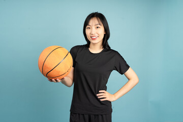 Young woman holds an orange basketball and smiles confidently in a black sports outfit against a...