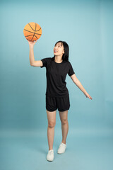 Fototapeta premium Young Asian woman in athletic wear gracefully holding a basketball while standing against a solid blue background