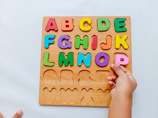 Child hand playing with colorful wooden alphabet puzzle board for early learning and education on...
