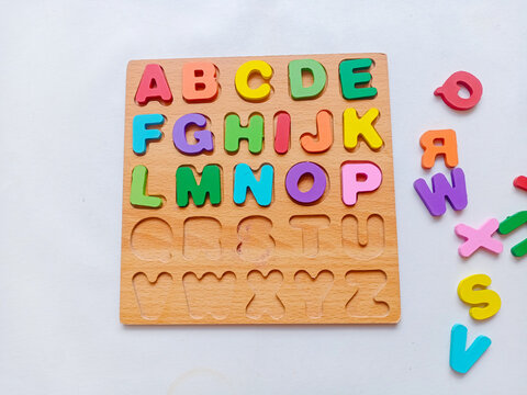 Child hand playing with colorful wooden alphabet puzzle board for early learning and education on white background.