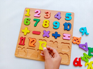 Asian child hand playing colorful wooden number puzzle board with math symbols for early learning