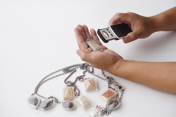 Close up man hand examines a Buddhist amulet using magnifying glass. Concept delicate art of sacred...