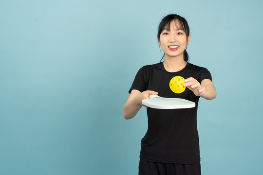 Person in black shirt demonstrating how to hold a pickleball paddle with a yellow ball in front of a light blue background