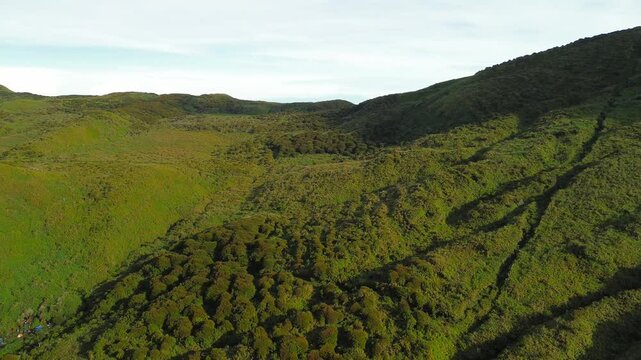 Camera circles the second campsite below Mount Apo, revealing undulating grass hills, a bowl-shaped basin and dense forest patches glowing in clear morning light.