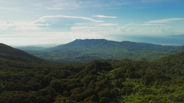 High above Mount Apo&rsquo;s slopes, the lens pushes forward across dense forest canopies toward a saw-toothed ridge and the shimmering Davao Gulf, all framed by crisp blue sky and cotton clouds.