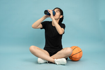 Young woman sits on the floor, enjoying a refreshing drink while relaxing next to a basketball on a...