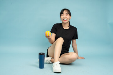 Young woman sitting on the floor holding a yellow ball, dressed in a black athletic outfit, in a...