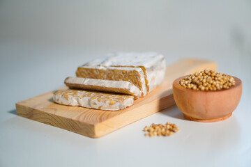 Tempeh that has been cut into pieces on a wooden chopping board with added coriander as a complement.