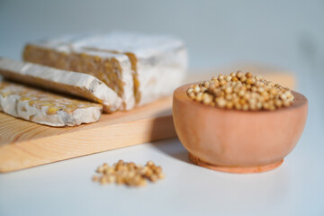 Tempeh that has been cut into pieces on a wooden chopping board with added coriander as a complement.