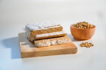 Tempeh that has been cut into pieces on a wooden chopping board with added coriander as a complement.