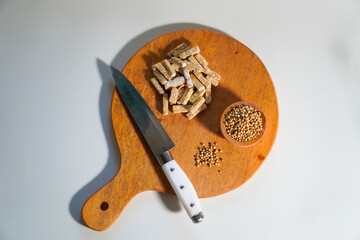 Tempeh that has been cut into small pieces on a wooden chopping board, complete with a knife and a...