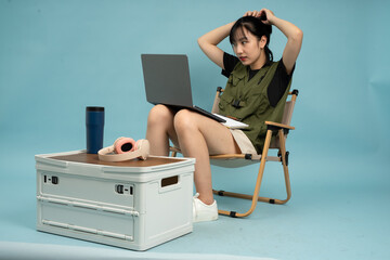 Woman working on a laptop in a casual setting with a blue background while adjusting her hair in a...