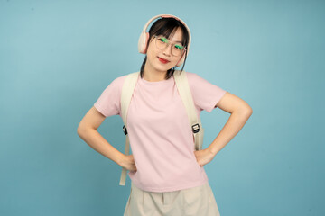 A young Asian woman smiles and gestures upward with her finger while wearing headphones and a...