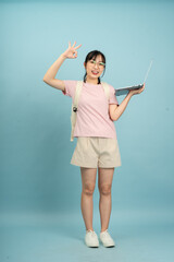 Young girl smiles while showing peace sign and holding laptop against a blue backdrop in a playful...