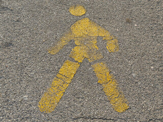 Yellow pedestrian symbol on asphalt: weathered street art for safe walking paths