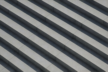 Repetitive pattern of concrete steps in diagonal view with strong shadows, creating a minimal and geometric architectural composition.