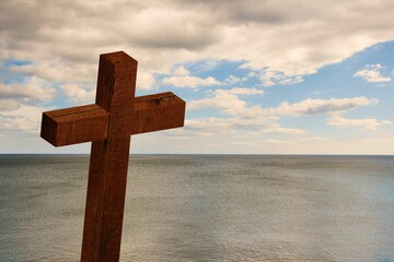 Flat design weathered wooden cross is standing on left side overlooking calm sea under cloudy sky