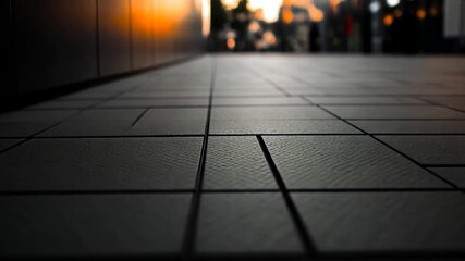 Ground-level view of a gray tile pathway leading toward a blurred cityscape at sunset. The perspective emphasizes the geometric patterns of the tiles against a warm orange glow on the buildings in - Powered by Adobe