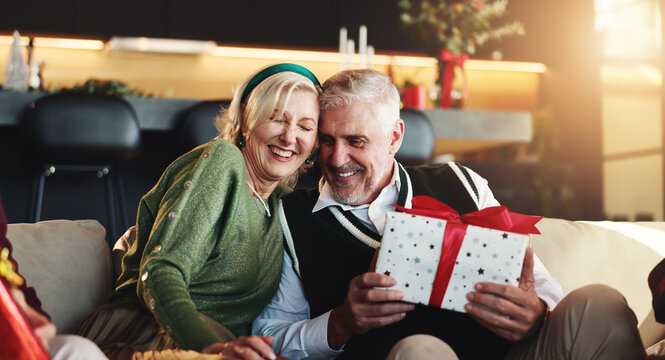 Christmas, hug or senior couple with gift for retirement, support or festive celebration. Care, smile or woman giving xmas present for gratitude, elderly man or love for holiday tradition in home - Powered by Adobe