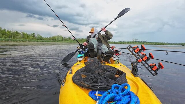 Kayak fishing, angler paddling in fishing pdl kayak during storm wind gust in weedy lake pond. Sport and bass fish tournament activity on pedaling fishing kayak. Water hobby and active lifestyle.