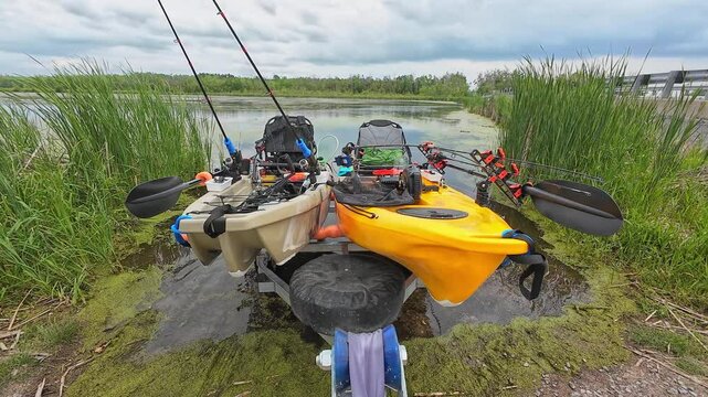 Fishing kayaks prepared for the launch and fishing at the lake. Boat trailer at the ramp water access attached to the truck hitch mount and fishing pedal kayaks. Sport fish tournament at spring.