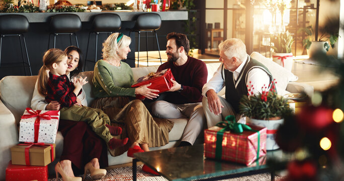 Grandparents, parents and child with gift for Christmas, festive season and bonding on holiday. Happy family, home and girl with mom, dad and senior people for tradition, celebrate or giving presents