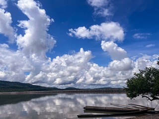 Wooden boats at the calm reservoir with cloud reflections and mountain background.