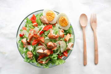 A cesar salad bowl filled with lettuce, tomatoes, egg and chicken. The salad is served in a clear glass bowl