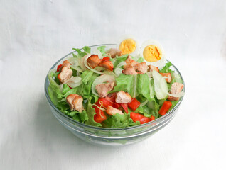 A cesar salad bowl filled with lettuce, tomatoes, egg and chicken. The salad is served in a clear glass bowl