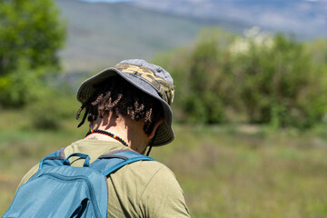 Caucasian man with cap and backpack walking through a mountain meadow during summer vacation