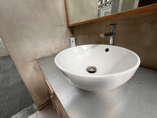 Fototapeta premium A white porcelain sink with a chrome faucet sits on a countertop. The sink is surrounded by a mirror and a toilet paper dispenser. The bathroom has a modern and clean aesthetic