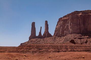 Fototapeta premium The Three Sisters spires in Monument Valley on the Colorado Plateau, Arizona. De Chelly Sandstone with Organ Rock Formation / Shale. A mesa is a flat-topped mountain or hill. Mitchell Mesa. Pinnacle