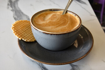 A cup of coffee with foam and a cookie