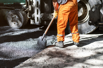 Construction worker lays asphalt on a sunny day in a busy urban area with heavy machinery nearby