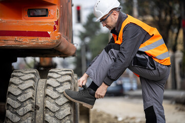 Construction worker adjusts boots before operating heavy machinery at a worksite in the city