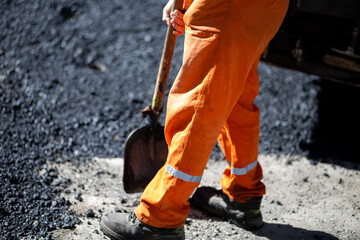 Construction worker shoveling asphalt in orange overalls on a sunny day