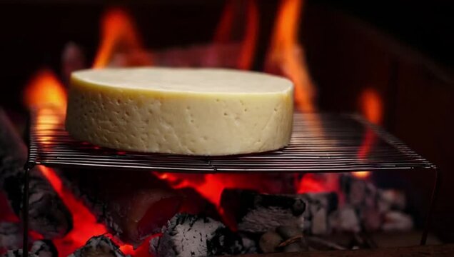 A piece of cheese slowly melting over an open flame. Hot embers create a cozy ambiance reminiscent of a fireplace or barbecue, highlighting the natural texture and appetizing appearance of the cheese.