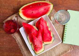 watermelon slices on a white porcelain serving plate and a glass of water and rosella tea for a...