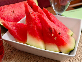 close up watermelon slices on a white porcelain serving plate and a glass of water