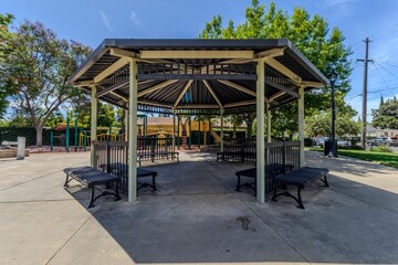 Gazebo in a park with benches and trees under a clear blue sky.