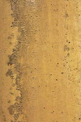Thin paint layer on weathered rustic concrete displays rough, corrugated surface with scattered holes. Uneven textures create mountain range like line between varying shades of orange and tan brown.