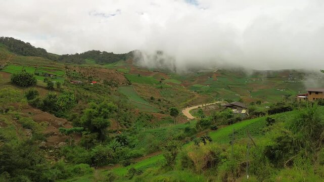 Terraced vegetable plots, scattered farmhouses and a winding dirt road blanket Mount Apo&rsquo;s foothills, while dense cloud banks drift just above the green-brown slopes.
