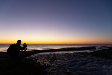 A photographer takes a picture of a river at sunrise.