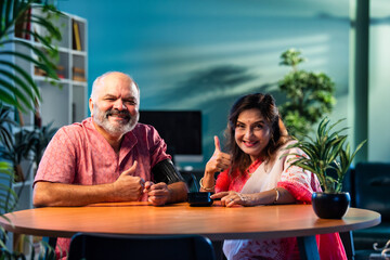 Indian senior couple using BP monitor at home, pleased with normal blood pressure reading