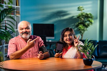 Indian senior couple using BP monitor at home, pleased with normal blood pressure reading