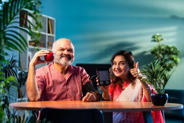 Indian senior couple using BP monitor at home, pleased with normal blood pressure reading